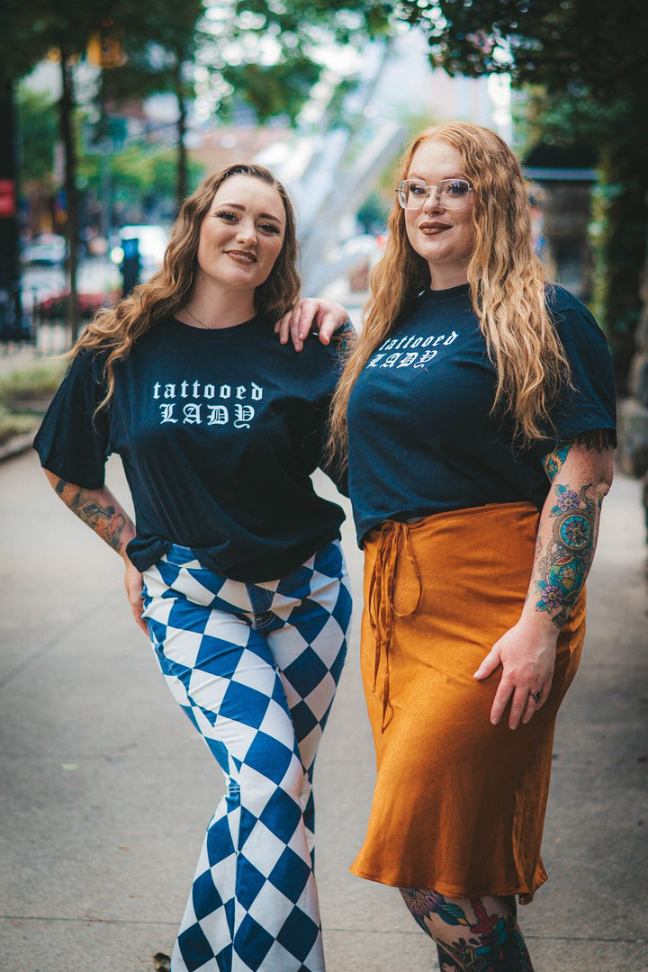 Two women wearing 'tattooed lady’ cropped tee standing on a sidewalk.